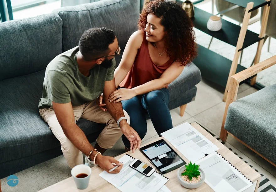 Couple sitting on a couch, making plans with documents and an iPad on the coffee table.
