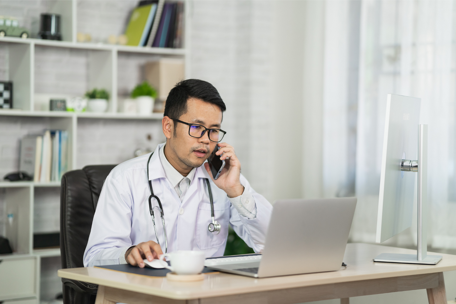 Male doctor speaks on the phone while working at his computer.