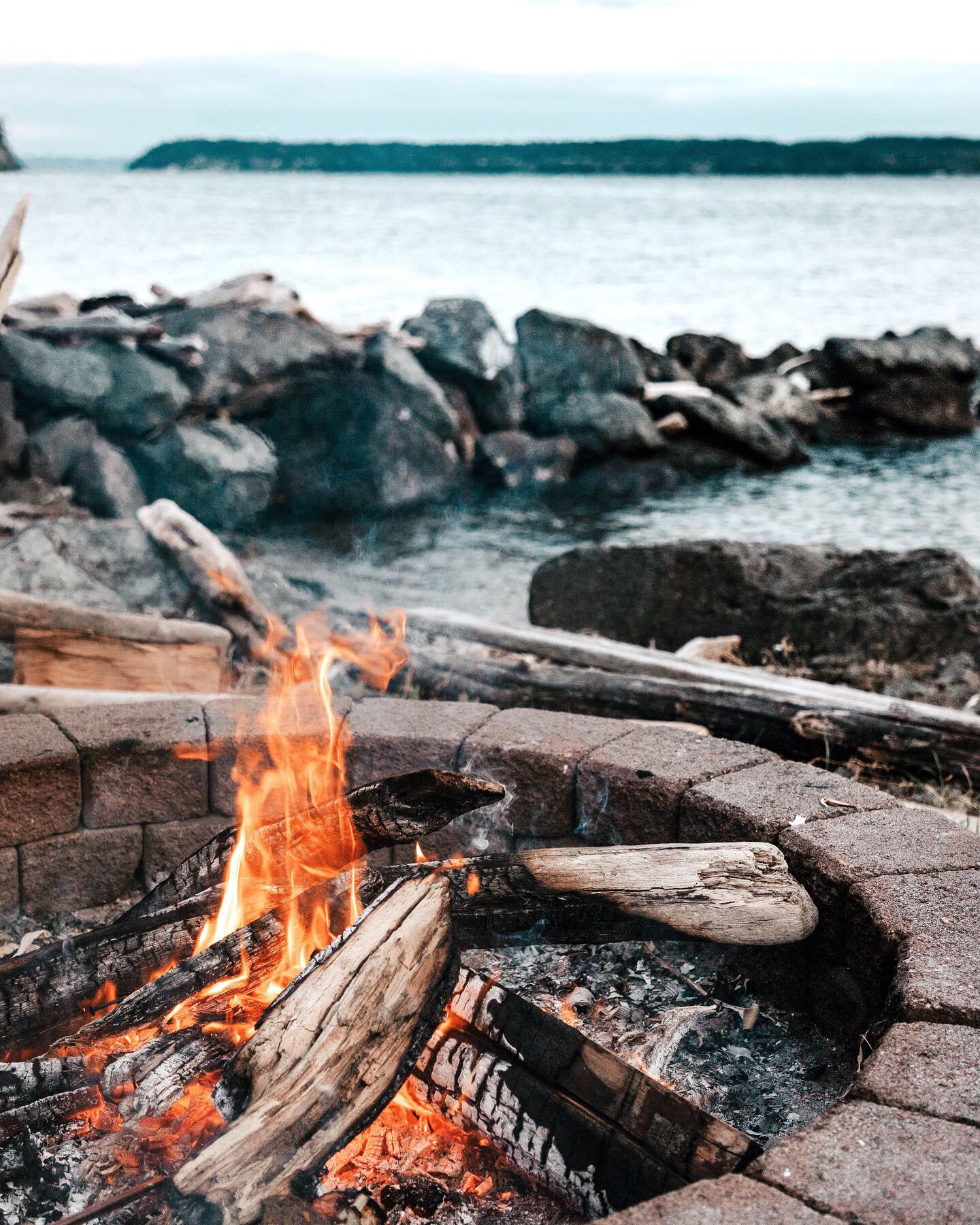 Fire burning in an outdoor firepit with lake in the background.