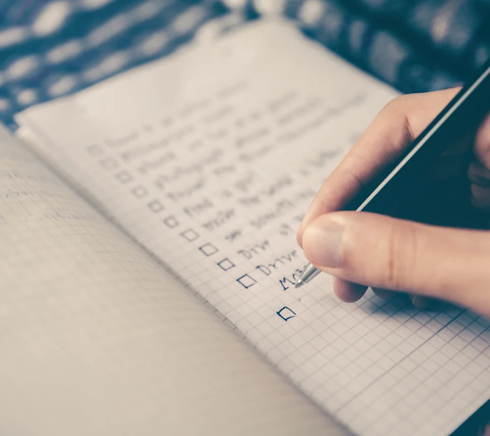 Hand writing a to-do list in a square-grid notebook. All list items are blurred.