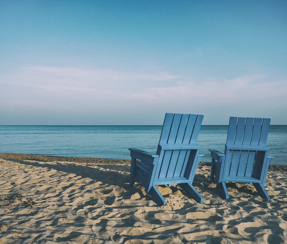 Two empty, blue chairs sit on a beach on a sunny day.